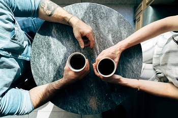 Looking down on a round table, two sets of arms hold coffee cups