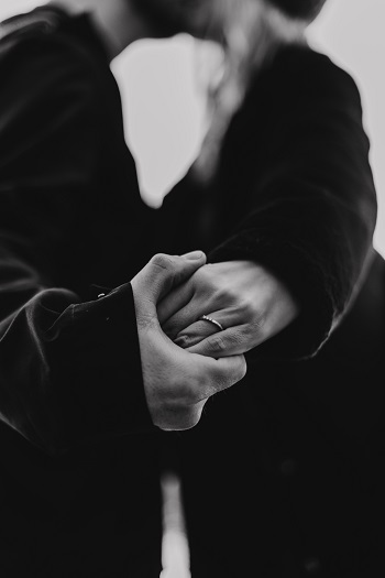 A couple holds hands while kissing, faces out of frame