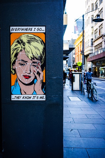 A cartoon image of a crying woman is posted on a wall beside a street. Text reads "Everywhere I go, they know it's me"