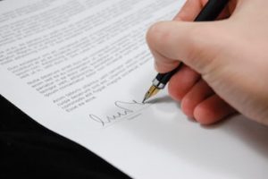 A hand signing a name on the signature line of a legal document.