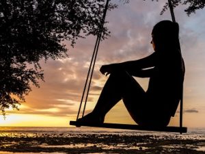A silhouette of a woman sitting in a rope swing