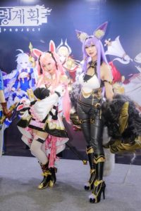 Two women cosplaying in a pink and purple wig and cosplay outfits.