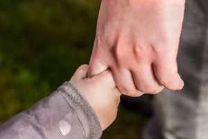 Small child's hand holding adult finger.