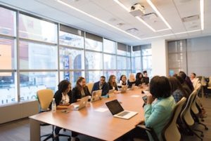 Women in a conference room, sitting around a long rectangular table.