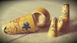 Three wooden Russian dolls on the ground, the largest one laying open on its side and subsequent smaller ones standing upright.