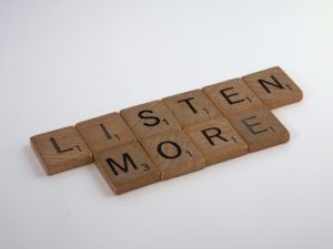 "LISTEN MORE" spelled out in Scrabble letter blocks, with a white backdrop.