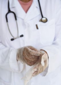 Doctor wearing stethoscope and pulling on plastic disposable gloves.