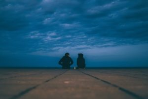 Two people sitting outside under a dark, blue, stormy sky.