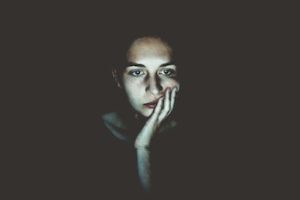 Anxious woman sitting with her face in her hand, with the white glow of a screen.