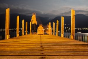 Person at the edge of a dock over the water, faded images of the person sitting, standing, and sitting a different direction.