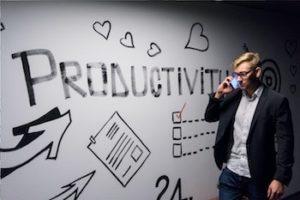 Man holding smartphone to ear standing next to artwork on a wall that includes the word 'PRODUCTIVITY' and hearts.