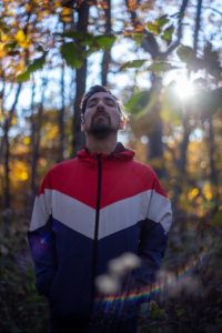 Man standing in the forest amid streaks of sun.