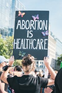 Woman holding up sign during protest that says "ABORTION IS HEALTHCARE".
