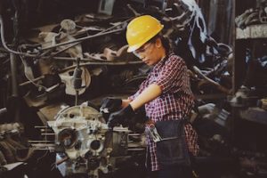 Woman in a yellow hard hat carrying out a task in the trades.