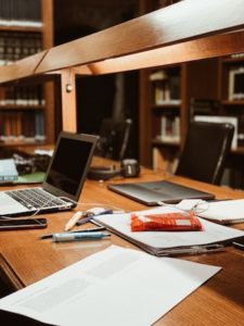 A desk in a library with laptops, stationary and a bag of candy.