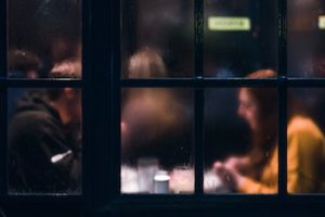 Looking in at patrons at a seated restaurant or cafe through a misty window.