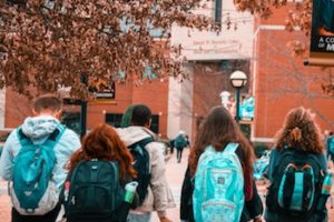 The backs of college students on campus as they walk toward a building.