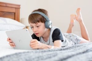 boy in black and grey shirt lays on bed and plays with iPad