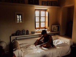 man sits on a bed with white sheets and looks sad