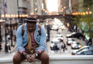 man sitting on a bench with a hat on and looks sad