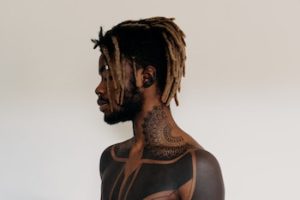 black man looking to the side showing all tattoos from neck down