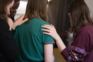 a group of three friends with their hands on the shoulders of the friend standing in the middle 