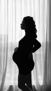Black and white silhouette of a pregnant woman standing in a window