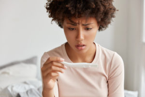 Frustrated young woman cant get pregnant, complains of bad results on pregnancy test, sits on bed, wears casual clothes, poses against cozy domestic interior. Feminity and fertility concept.