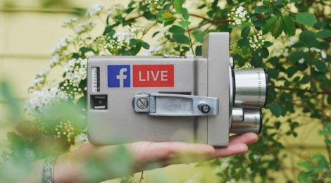 A video camcorder held in a hand with a Facebook logo on it.