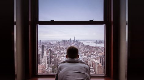 A man, facing away, stares out at a cityscape