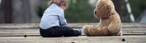 A small boy sitting with a teddy bear on a wooden bridge.
