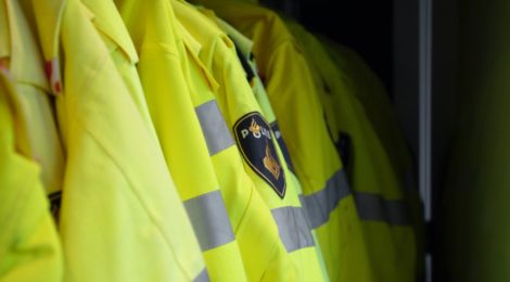 Yellow police jackets lined up and hanging on a clothing rack.