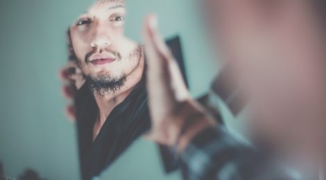 Man holding broken shard of mirror and looking at his reflection.