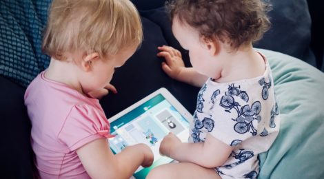 Two young children sitting on the couch engaging with an electronic tablet.