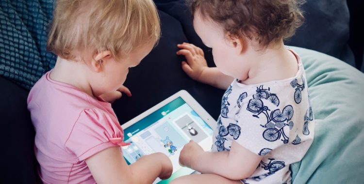 Two young children sitting on the couch engaging with an electronic tablet.