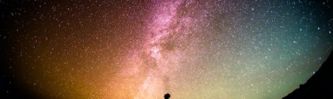 Profile silhouette of a person standing beneath a colourful night sky full of stars.