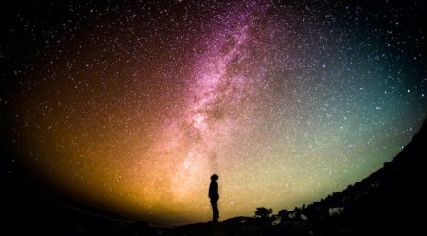 Profile silhouette of a person standing beneath a colourful night sky full of stars.