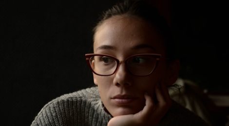 Woman wearing glasses resting her head in her hand and looking sideways.