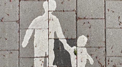 White painted silhouette of parent and child hand-in-hand on a grey brick sidewalk.