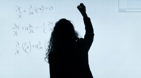 Silhouette of a woman writing mathematical equations on a whiteboard.