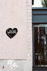 a black heart on a pink wall that reads you are beautiful