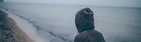 person in hoodie looks out across a lake