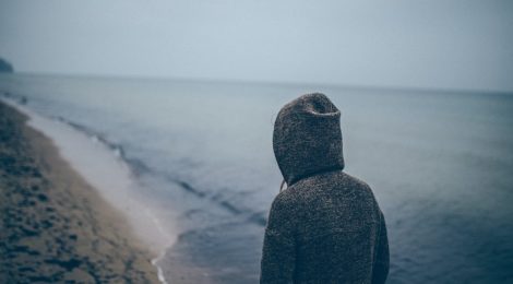 person in hoodie looks out across a lake