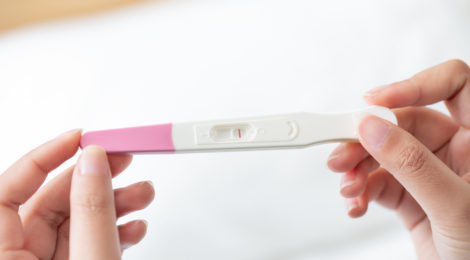 A closeup of a woman's hand holding up a pregnancy test kit with a negative result