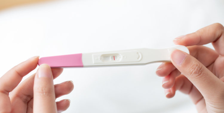 A closeup of a woman's hand holding up a pregnancy test kit with a negative result